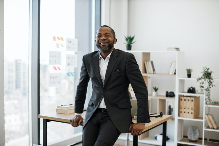 Company leader resting on edge of office desk